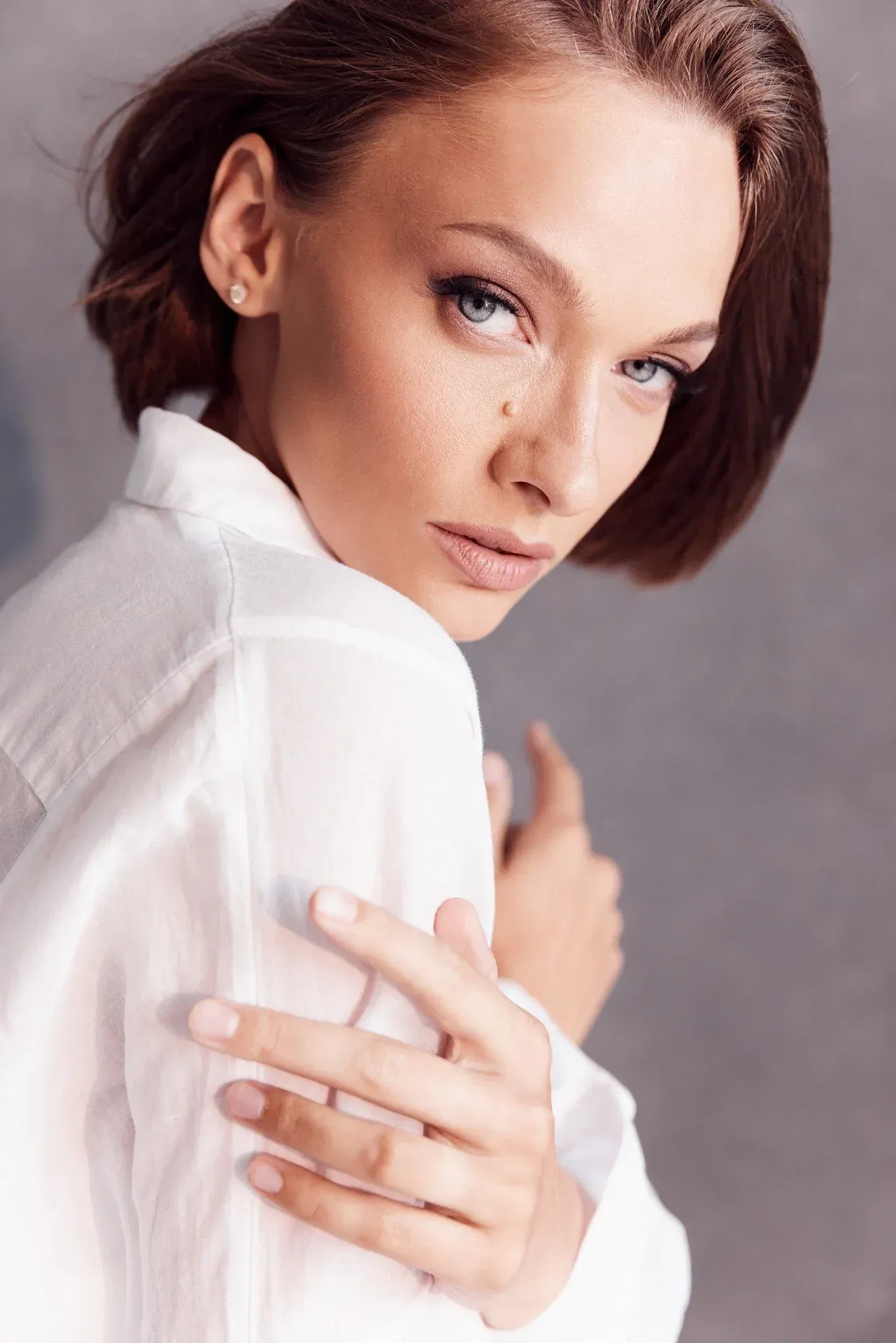 Une femme aux cheveux courts brun-roux, aux yeux bleus, vêtue d'une chemise blanche, regarde directement la caméra, les bras croisés sur la poitrine.